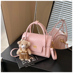 Detail einer rosa Handtasche mit Goldlogo, Teddybär-Anhänger und Schultergurt-Detail