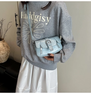 Detail shot of light blue crossbody square bag with metal buckle and zippers on model
