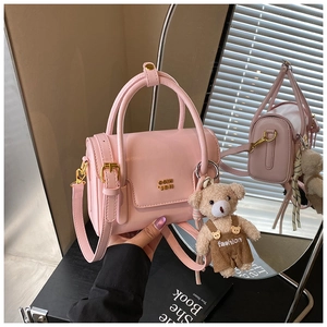 Detailansicht der rosa Ledertasche mit Goldlogo, Schultergurt und Plüschbär-Anhänger