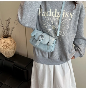 Detail view of light blue crossbody bag with metal ring buckle and decorative zippers