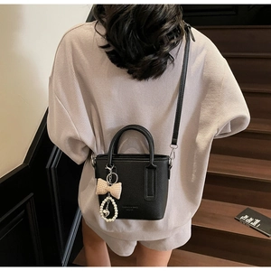 Detail of black lychee leather bucket bag with elegant pearl and bow charm accessory