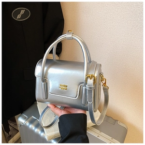 Detailaufnahme der silbernen Handtasche mit goldenem Logo und Ledergriff