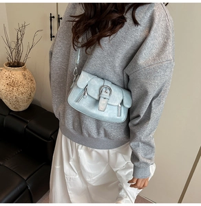 Detail of light blue faux leather crossbody bag with metal buckle on a model