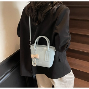 Detail of light blue bucket bag with pebble texture and pearl bow charm accessory
