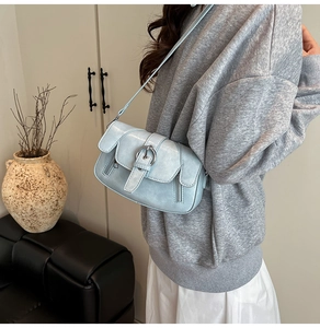 Close-up of light blue leather crossbody bag with metal buckle and side zipper detail