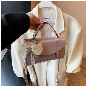 Dettaglio borsa in pelle viola chiaro con ciondolo a cuore di perle e fiocco di pizzo
