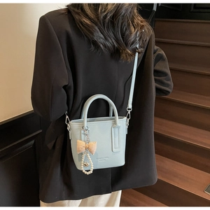 Detail of light blue leather bucket bag featuring bow and pearl heart charm accents