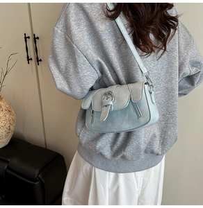 Detail view of a gray-blue crossbody bag with silver buckle and side zipper decorations