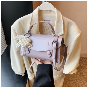 Dettaglio borsa lilla con fiocco in pizzo e ciondolo di perle su blazer beige