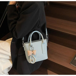 Detail of light blue bucket bag with leather texture and pearl bow charm accessory