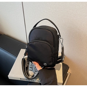 Détail du sac bandoulière en nylon noir avec large sangle tissée et compartiments zippés