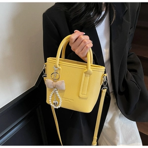 Detail of yellow lychee texture leather tote bag with pearl bow charm and shoulder strap
