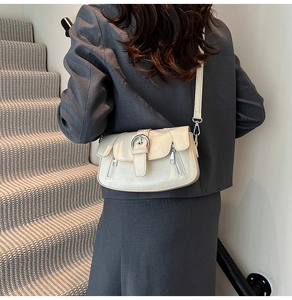 Detailed back view of minimalist cream leather crossbody bag with silver buckle on a model
