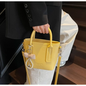 Detail of yellow bucket bag with lychee texture leather and a heart pearl charm