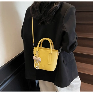 Detail of yellow pebbled leather bucket bag with bow pearl charm on black blazer