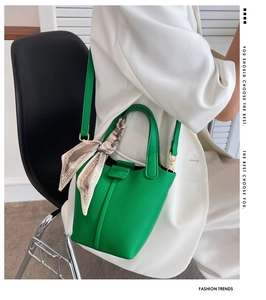 Detail of green leather bucket bag with silk scarf on handle and model wearing white blazer