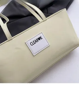 Detail shot of cream patent leather bag showing square CLEAR♥K logo patch and soft texture