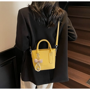 Detail view of yellow litchi pattern leather bucket bag with pearl bow charm on stairs