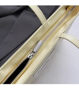 Close-up of smooth silver zipper and metal puller on creamy yellow glossy leather bag