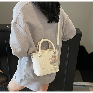 Detail of cream white leather bucket bag showing grain texture and decorative bow charm