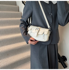 Detail of ivory small square crossbody bag with round metal buckle and zipper on model