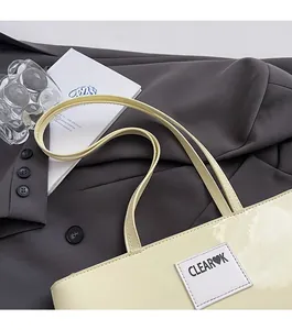 Detail of butter yellow patent leather tote bag featuring a brand logo and slim shoulder straps