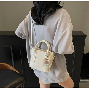 Detail of cream-white lychee textured bucket bag with bow and pearl charm pendant