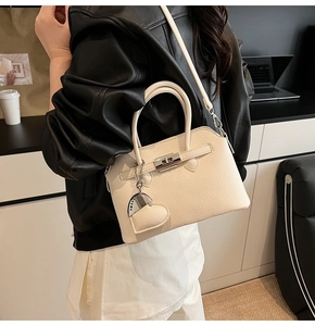 Detail van een crèmekleurige leren handtas met zilveren slot en hartvormige hanger