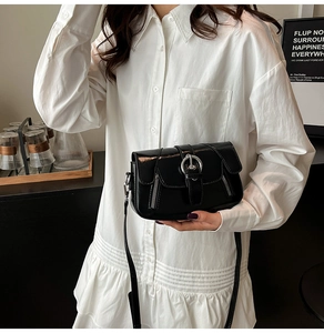 Detail of black glossy crossbody bag with metallic round buckle and decorative zippers