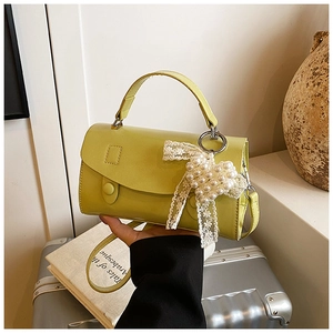 Dettaglio borsa verde in pelle con ciondolo a cuore di perle e fiocco in pizzo