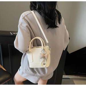 Detail of a creamy white leather bucket bag featuring a pearl charm and plaid bow