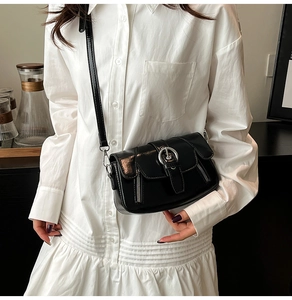 Close-up of black glossy mini crossbody bag with silver round buckle and metal zippers