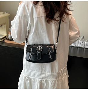 Close-up of black crossbody bag with silver buckle and decorative zippers on model