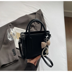 Macro shot of black litchi pattern leather handbag with pearl charm and bow detail
