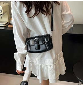 Detail of a black glossy PU leather crossbody bag with silver buckles and zippers on a model