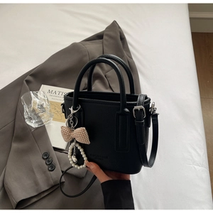 Detail of black pebbled leather bucket bag with fashion embossing and pearl bow charm