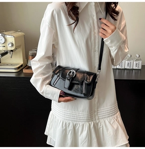Close-up of black glossy PU leather crossbody bag with vintage buckle and zipper details