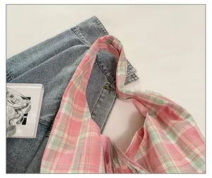Détail de la large bandoulière confortable sur un sac en toile à carreaux rose et vert