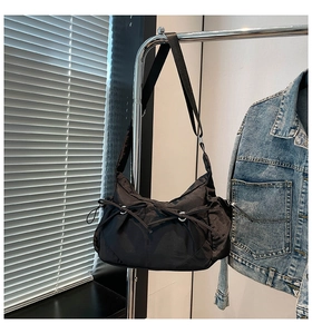 Détail d'un sac bandoulière en nylon noir avec laçage suspendu sur un cintre en métal