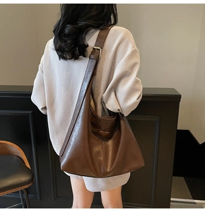 Detail of dark brown leather tote bag featuring a golden triangle logo and wide shoulder strap