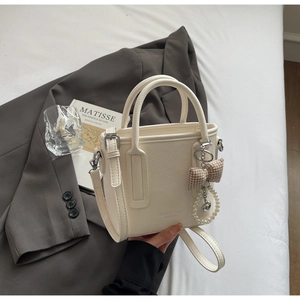 Close-up of white lychee pattern leather bucket bag with bow and pearl pendant details
