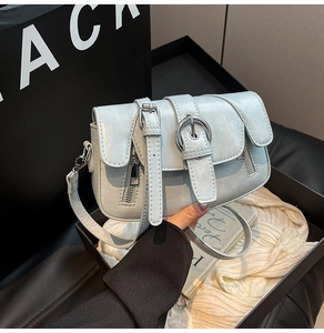 Detail of light blue crossbody bag with silver circular buckle and metallic zippers