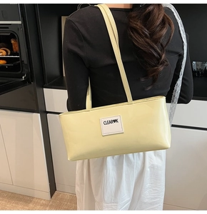 Pale yellow patent leather shoulder bag with CLEAR HEART K patch on a model back