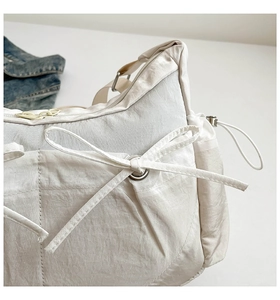 Détail du sac bandoulière en nylon crème avec nœud décoratif et texture plissée