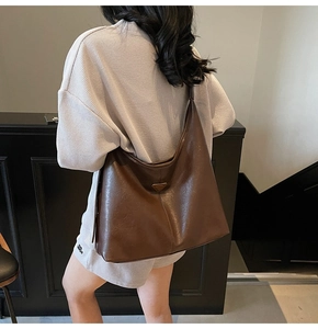 Detail of large dark coffee faux leather tote bag with iconic triangular metal logo emblem