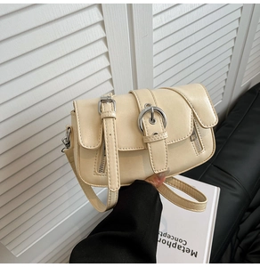 Detail shot of a beige faux leather underarm bag featuring decorative straps and dual zippers