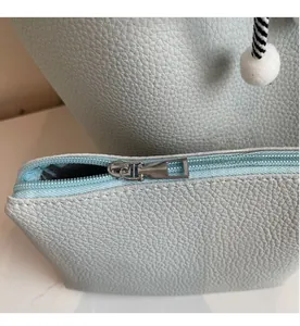 Detail of light blue lychee pattern leather pouch with silver zipper and fuzzy pompom
