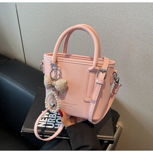 Detail of pink lychee leather handbag featuring a pearl bow charm and silver hardware