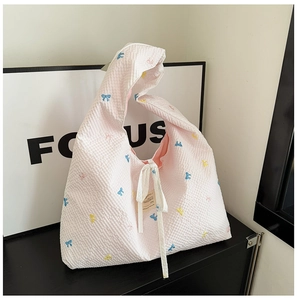 Détail d'un sac cabas rose gaufré avec broderies de nœuds colorés et ruban blanc