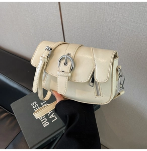 Close-up of cream underarm bag featuring silver round buckle and vertical strap details